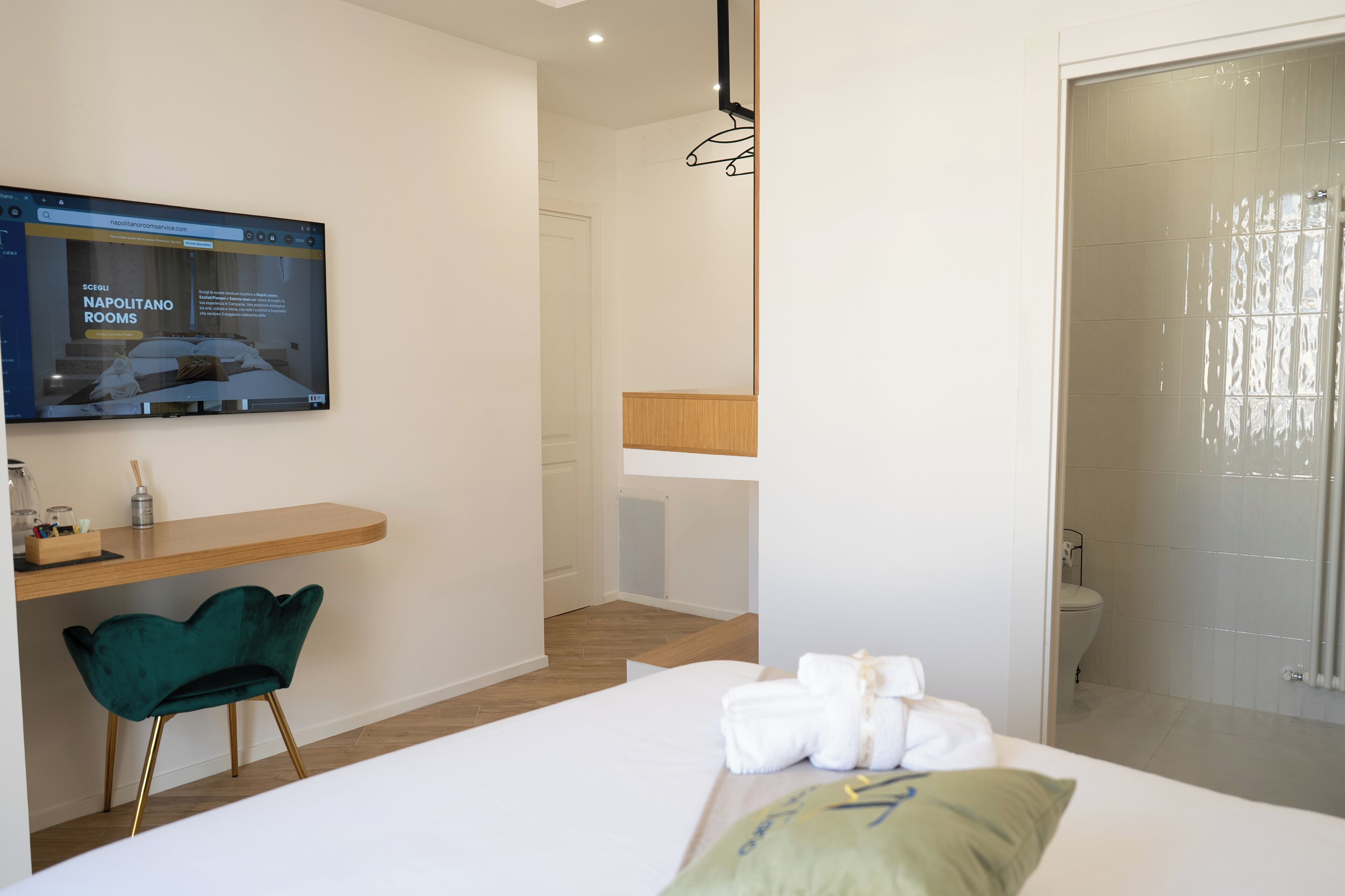 A hotel room with a bed, a desk with a computer, a chair, a bathroom, and a shower.