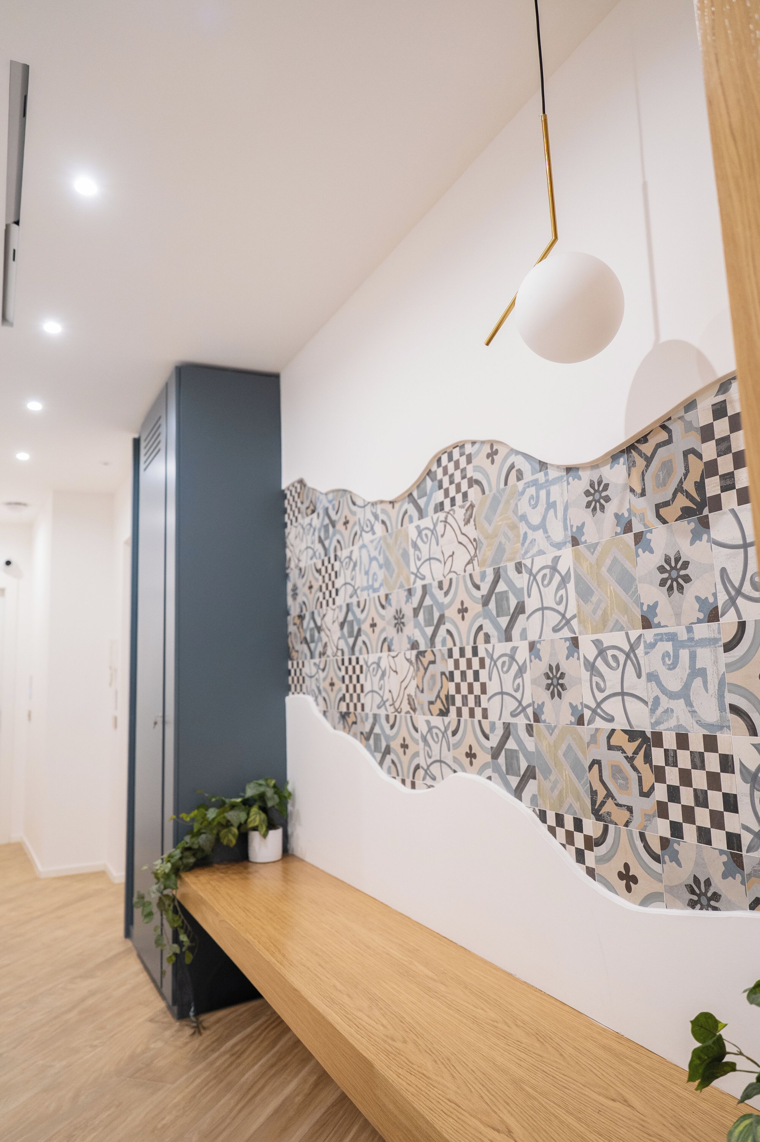 A hallway with patterned wall tiles, a wooden bench, a potted plant, and a hanging light fixture.
