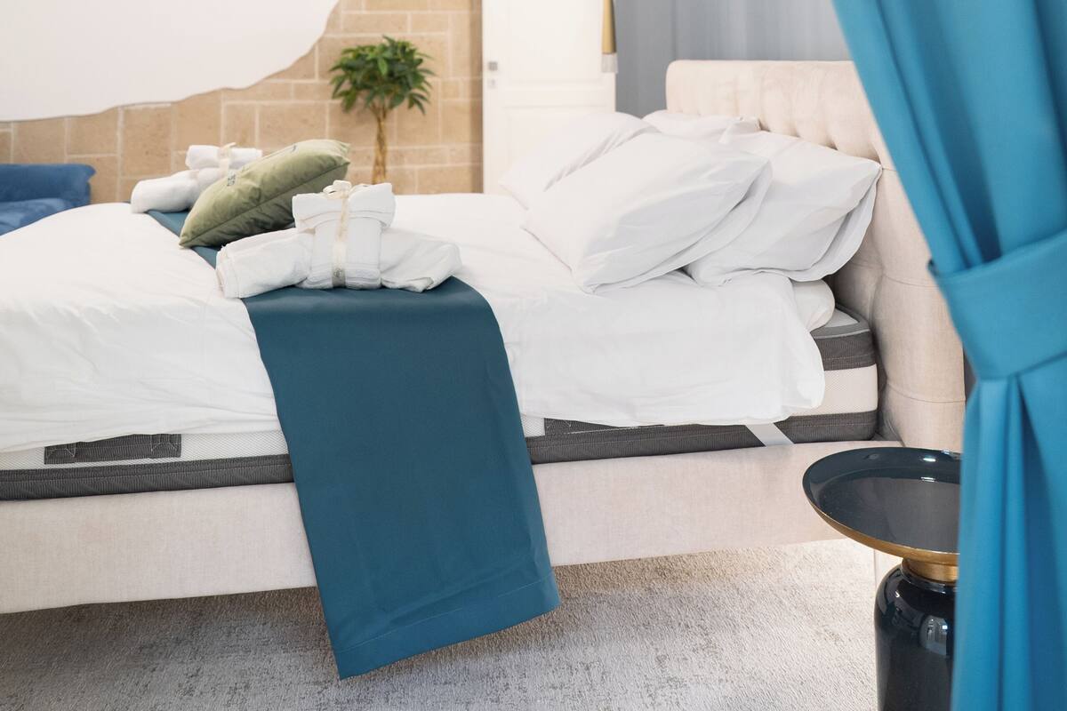 Quarto de hotel moderno com uma cama, uma mesinha e um aplique na parede.