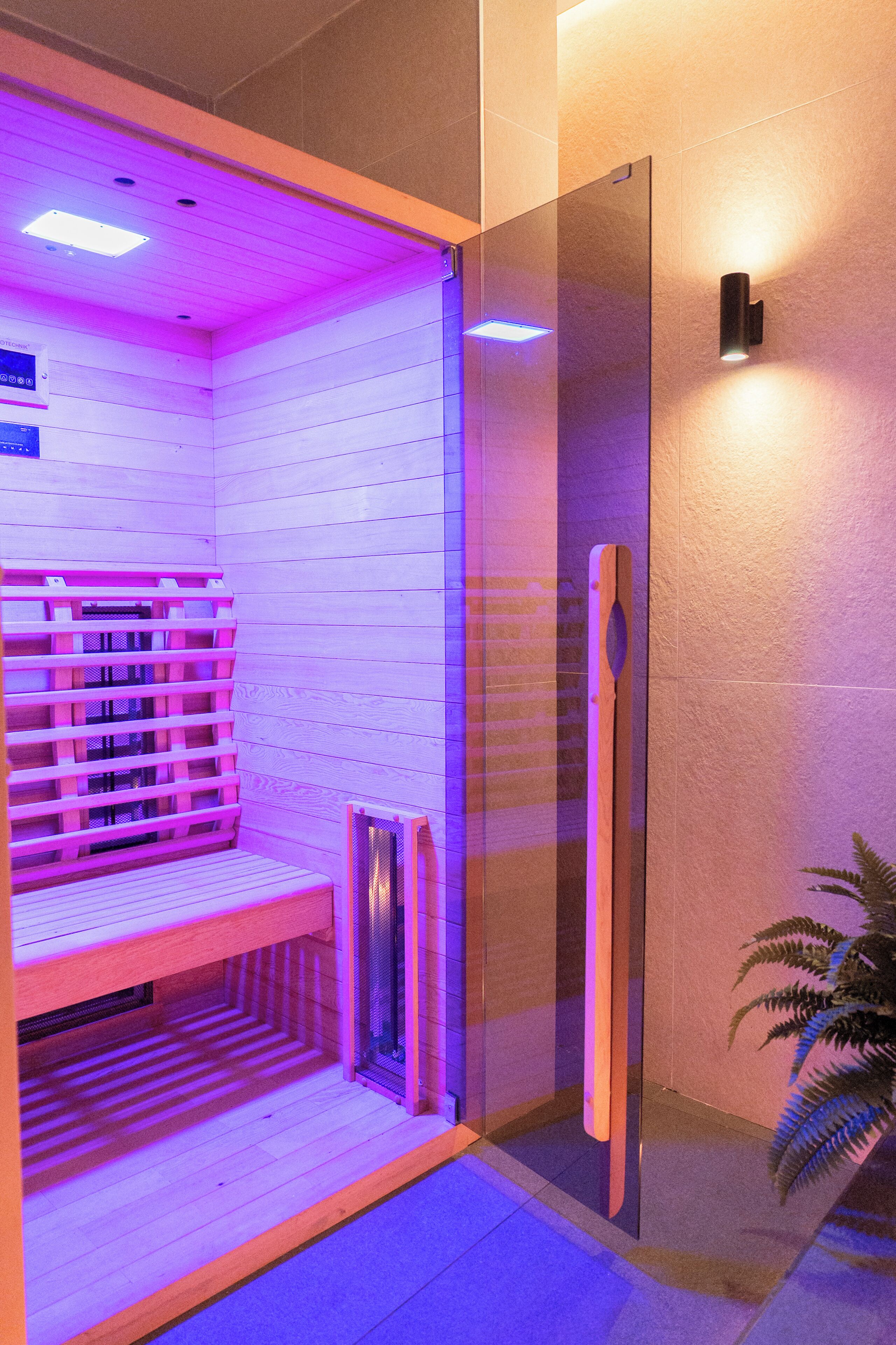 Un sauna équipé d’un banc, d’une porte en verre et d’un luminaire fixé au mur.