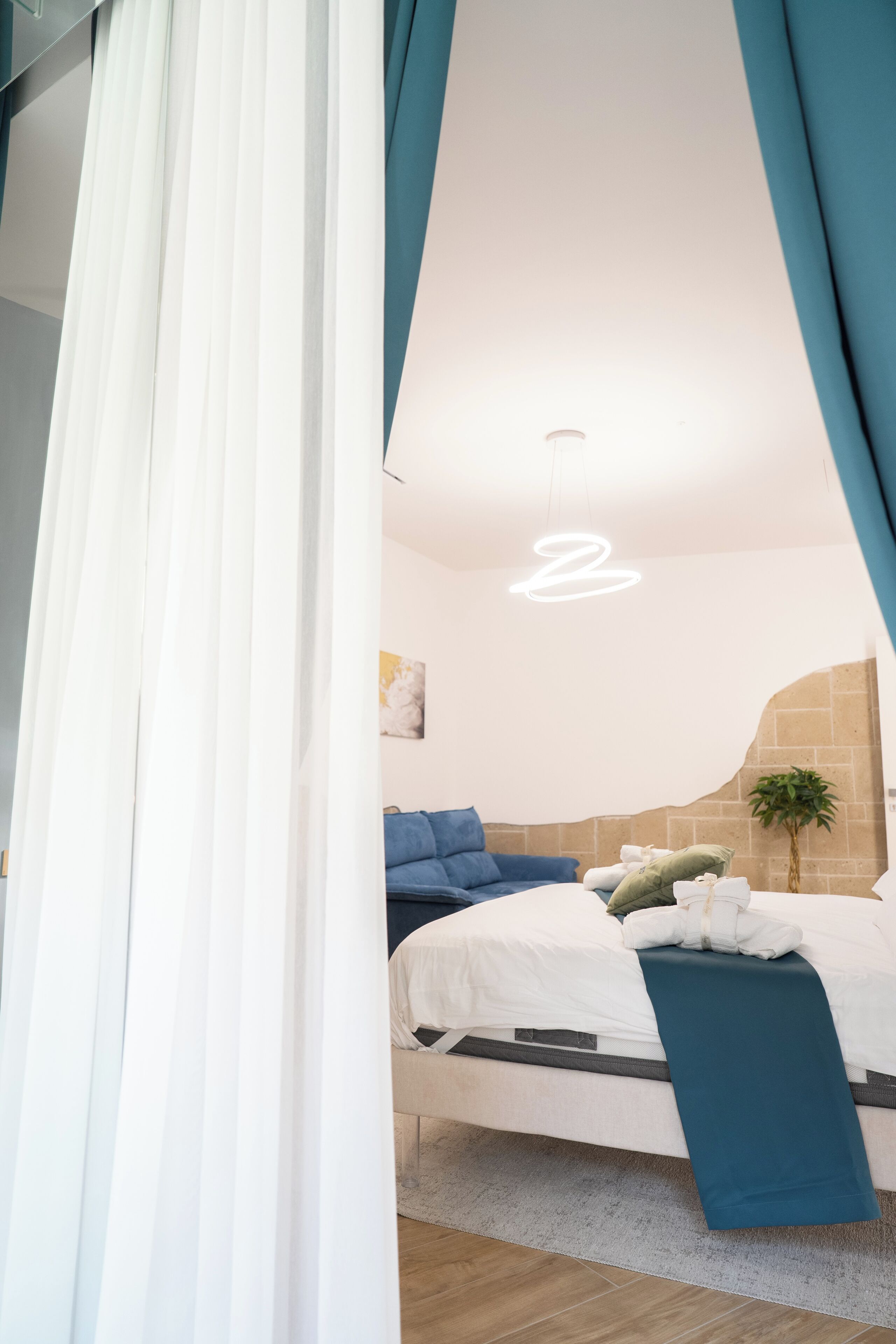 A bedroom with a bed, white curtains, a blue blanket, and a hanging light fixture.