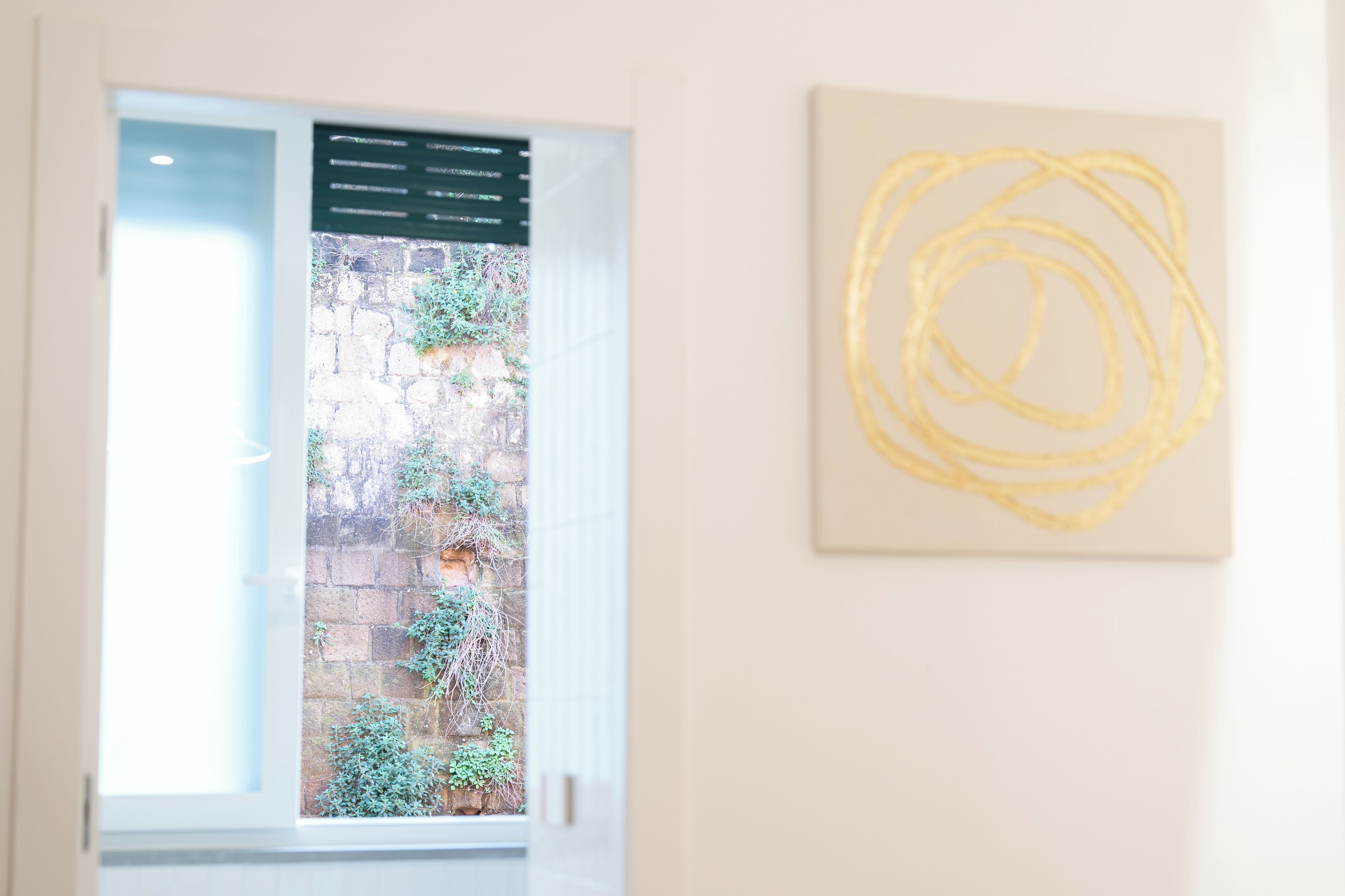 Una stanza con una finestra, una parete con un quadro astratto giallo e un muro in mattoni all'esterno.