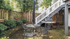 A patio with a round table and chairs, a grill, and a wooden fence. - Chapel Gate 3BR Steps to City Dock & Naval Academy (Annapolis)