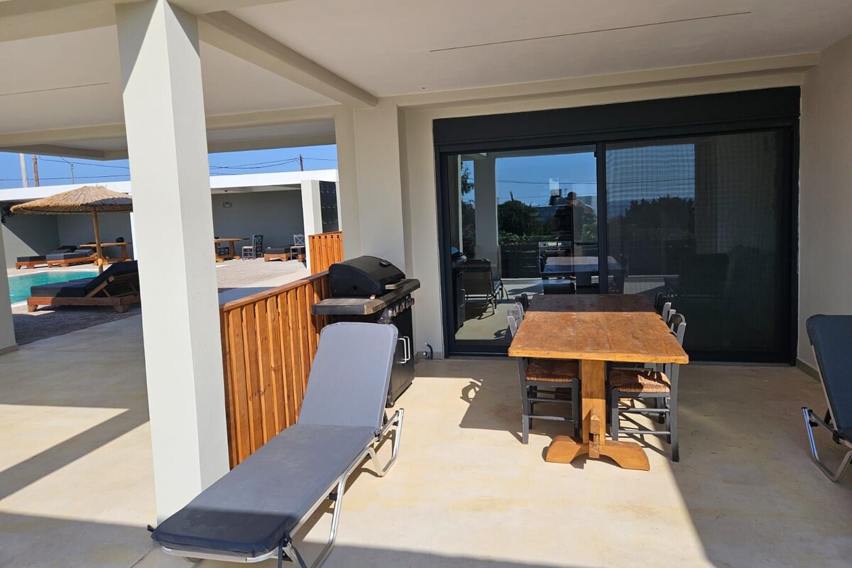 Un espace extérieur abrité comprenant une piscine, des chaises longues, un barbecue et une table avec des chaises.