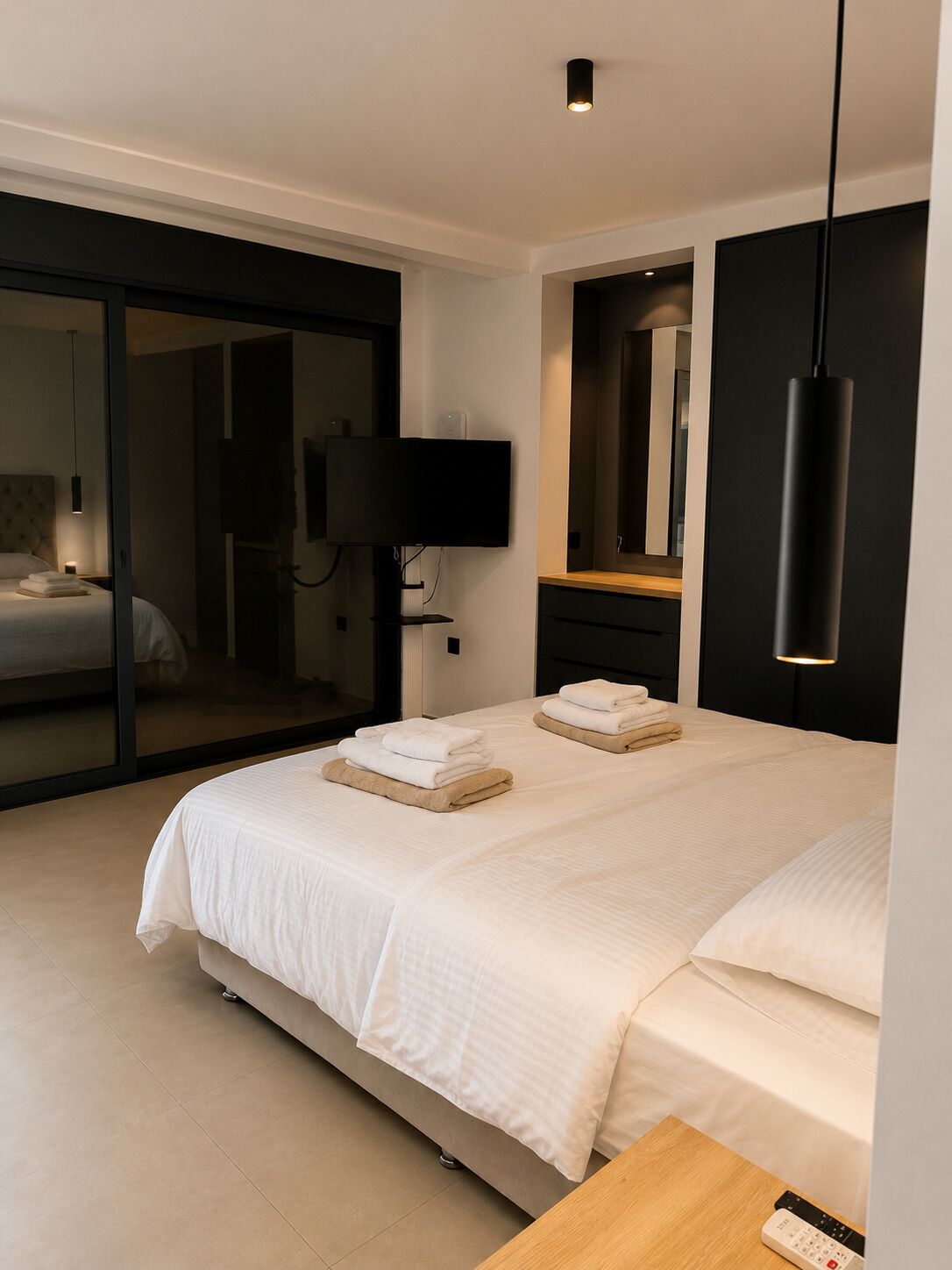 Una habitación de hotel moderna con una cama grande, un televisor de pantalla plana, un espejo y una puerta corredera que da al baño.