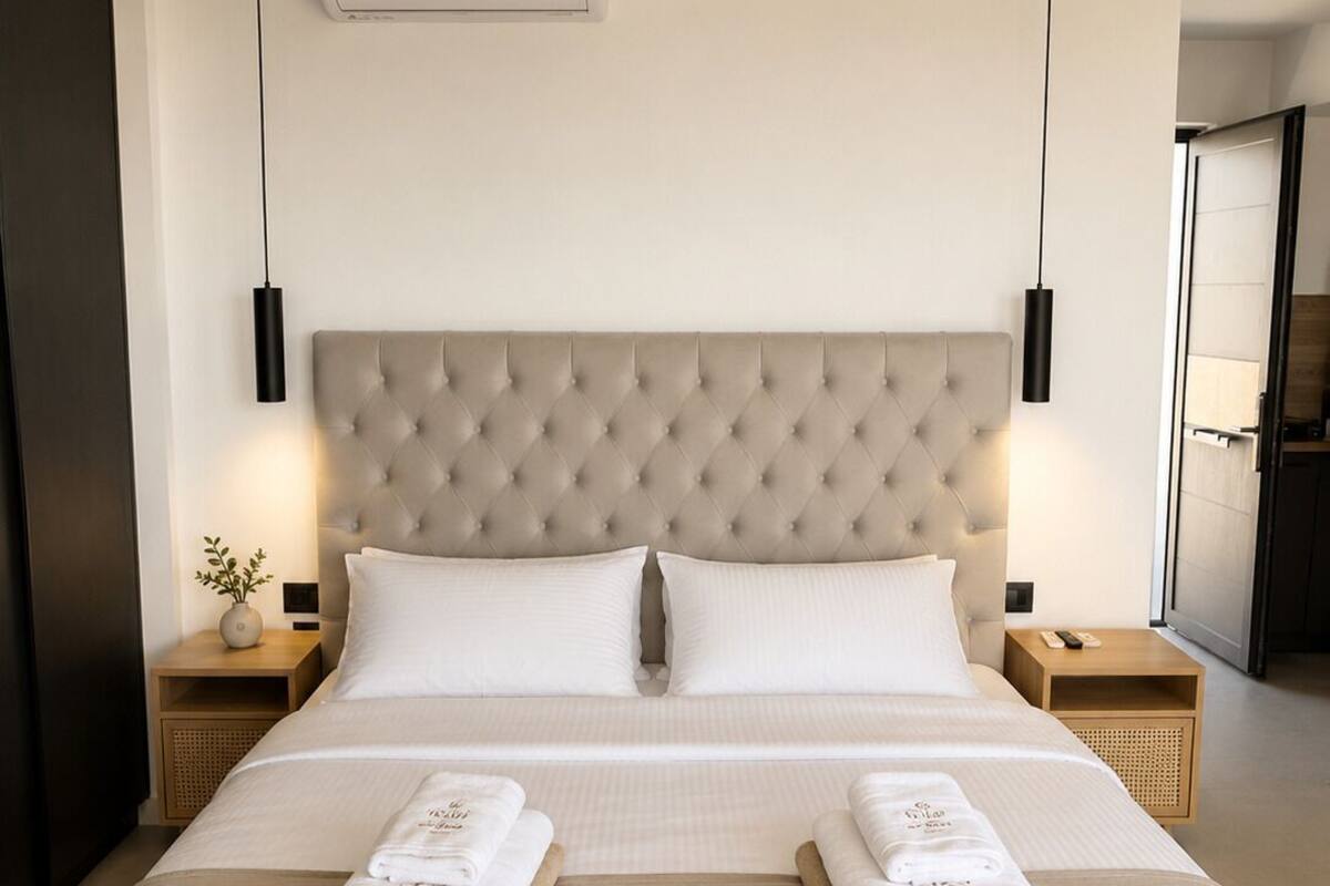 Habitación de hotel con una cama grande, dos mesitas de noche, aire acondicionado instalado en la pared y vista a la habitación contigua.