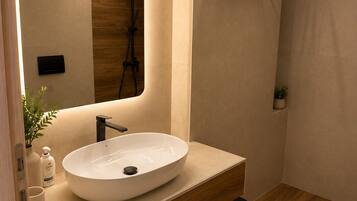A modern bathroom with a large oval sink, a mirror, a towel rack, and a shower area.