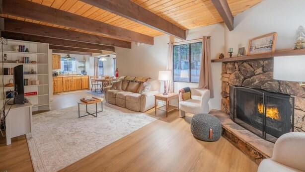 A spacious living room with a fireplace, wooden beams, a stone fireplace, and a view of the kitchen. - Big Bear Moonridge Escape (Big Bear Lake)