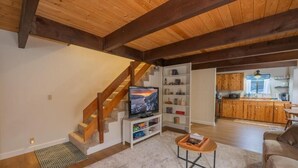 A living room with a wooden staircase, a television, a bookshelf, a kitchen area, and a sofa. - Big Bear Moonridge Escape (Big Bear Lake)
