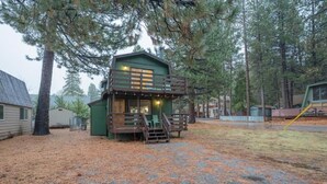 Una baita con una veranda in legno e scale che conducono a un balcone, immersa tra gli alberi.