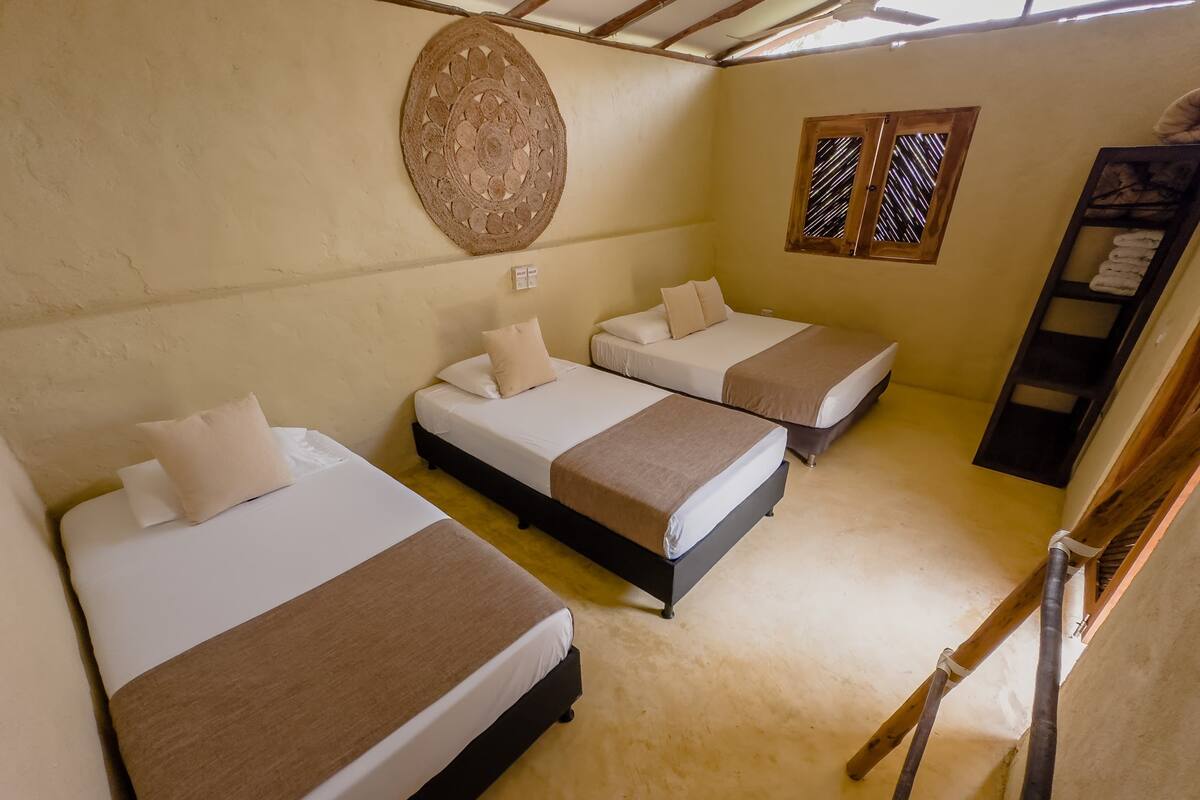 A room with three beds, a wall hanging, and a window with bars.