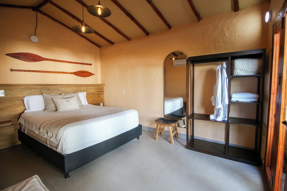 A bedroom with a bed, wooden headboard, two wooden stools, a shelf with towels, and two wooden paddles on the wall.