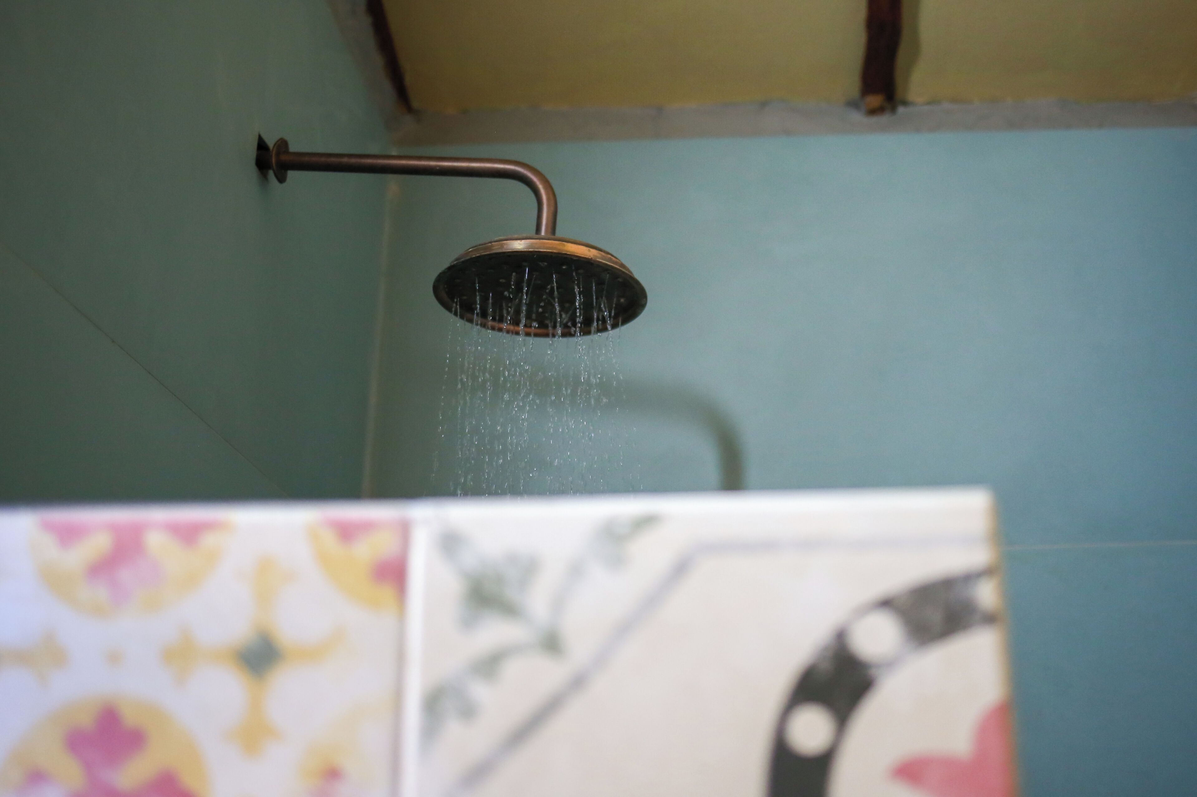 A showerhead with water running, mounted on a wall with a blue tile pattern.