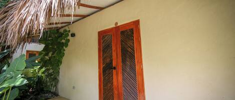 A building with a thatched roof, a wooden door with a window, and a small outdoor area with plants.