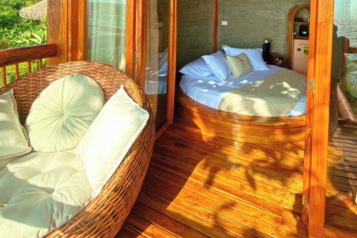 A wooden deck with a wicker sofa and a bed with pillows.