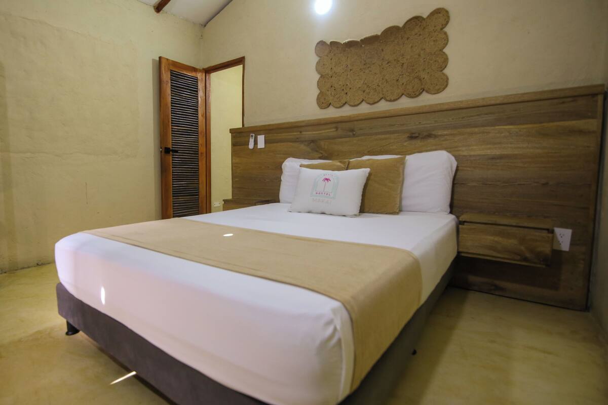A single bed with a wooden headboard, a beige bedspread, and a white pillow with a logo.