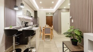 A modern kitchen with a dining area, featuring a central island, bar stools, and a potted plant.