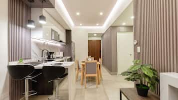 A modern kitchen with a dining area, featuring a central island, bar stools, and a potted plant.