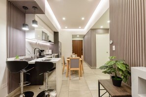 A modern kitchen with a dining area, featuring a central island, bar stools, and a potted plant.