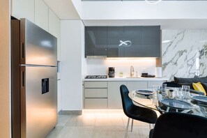 Une cuisine moderne dotée d’un réfrigérateur encastré, d’une cuisinière à gaz et d’un coin repas avec une table et des chaises en verre.