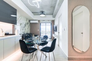 Une cuisine moderne avec un pare-feu en marbre, un coin repas doté d’une table en verre et de chaises noires, et un grand miroir accroché au mur.