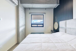 A bedroom with a bed, a window with a view of mountains, a bedside table with a mirror, and a wall-mounted air conditioning unit. - 1 Queen, 1 Sofa Bed, Wifi, Gym, Pool - 4 people (Monterrey)