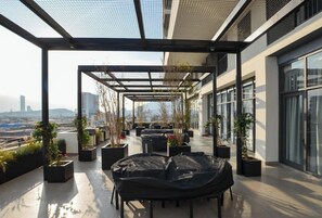 Une terrasse sur le toit, aménagée avec des espaces de détente en plein air, des plantes en pot et offrant une vue sur le paysage urbain.