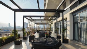 Une terrasse sur le toit, aménagée avec des espaces de détente en plein air, des plantes en pot et offrant une vue sur le paysage urbain.
