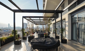 Eine Dachterrasse mit Sitzgelegenheiten im Freien, Kübelpflanzen und Blick auf die Stadt.