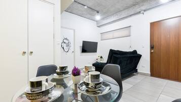A modern living space with a dining area, a black sofa, a TV mounted on the wall, and a wooden door.