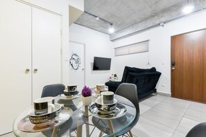 A modern living space with a dining area, a black sofa, a TV mounted on the wall, and a wooden door. - ¡Céntrico & Nuevo! 1 Queen Bed + Double Sofa Bed (Monterrey)