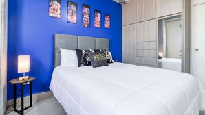 Ett sovrum med en blå vägg, en grå sänggavel, vita sängkläder och kuddar med Star Wars-motiv.