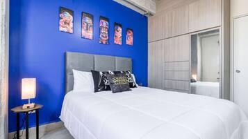 A bedroom with a blue wall, a grey headboard, white bedding, and Star Wars themed pillows.