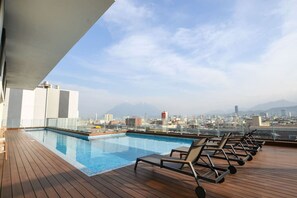 A rooftop pool with lounge chairs, a cityscape view, and a clear sky.