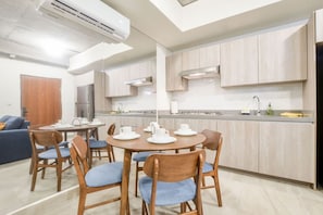 A modern kitchen with wooden cabinets, a dining area with a round table and chairs, and a built-in oven.