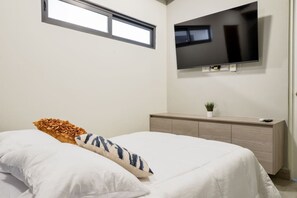 Un dormitorio con cama, televisor montado en la pared, ventana y aparador de madera.