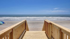 A wooden boardwalk leading to a beach with a clear sky.