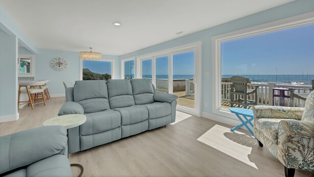 A spacious living room with a large gray sofa, a small round table, and a view of the ocean through large windows.
