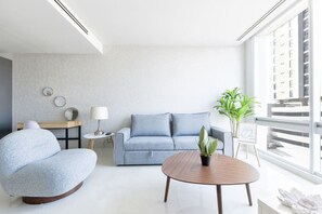 Ein modernes Wohnzimmer mit einer Couch, einem runden Couchtisch, einem Sessel, einem kleinen Tisch mit einer Lampe und einer Topfpflanze.