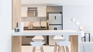 Eine moderne Küche mit weißer Arbeitsplatte, Edelstahlgeräten und einer Wand in Holzoptik.