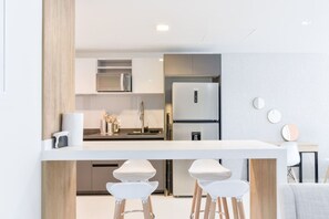 Eine moderne Küche mit weißer Arbeitsplatte, Edelstahlgeräten und einer Wand in Holzoptik.
