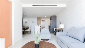 Ein modernes Wohnzimmer mit einer Couch, einem Couchtisch mit Pflanze, einem Essbereich mit Stühlen und einer Küche im Hintergrund.