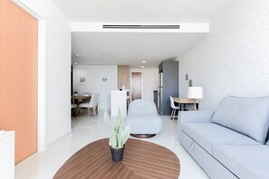 Ein modernes Wohnzimmer mit einer Couch, einem Couchtisch mit Pflanze, einem Essbereich mit Stühlen und einer Küche im Hintergrund.