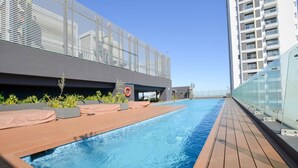 Ein Pool auf dem Dach mit Glasgeländer, einer Rettungsboje und einem modernen Gebäude im Hintergrund.