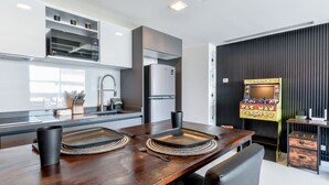 A modern kitchen with a dining table, chairs, a refrigerator, and a Pac-Man arcade machine. - ¡Loft in Santa Lucía! 3 guests, GYM, Pool, Parking (Monterrey)