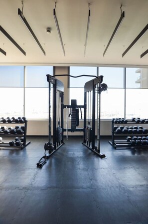 A gym with weightlifting equipment, dumbbells, and a large window.