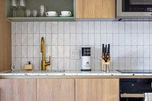 A kitchen with a white tiled backsplash, a gold faucet, a bottle of hand soap, and a dish rack with glasses. - Upscale 1BD Condo in Miami- City Views (Miami)