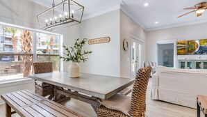 Een modern interieur met een eettafel, stoelen, een vaas met groen, een bord met de tekst 'BEACH HOUSE' en een schilderij van een landschap.