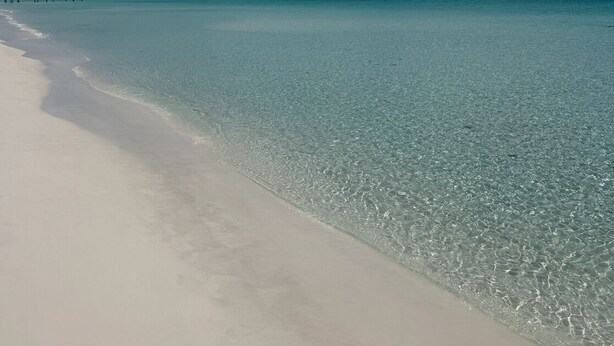 Een strand met helder turquoise water en een witte zandkust.