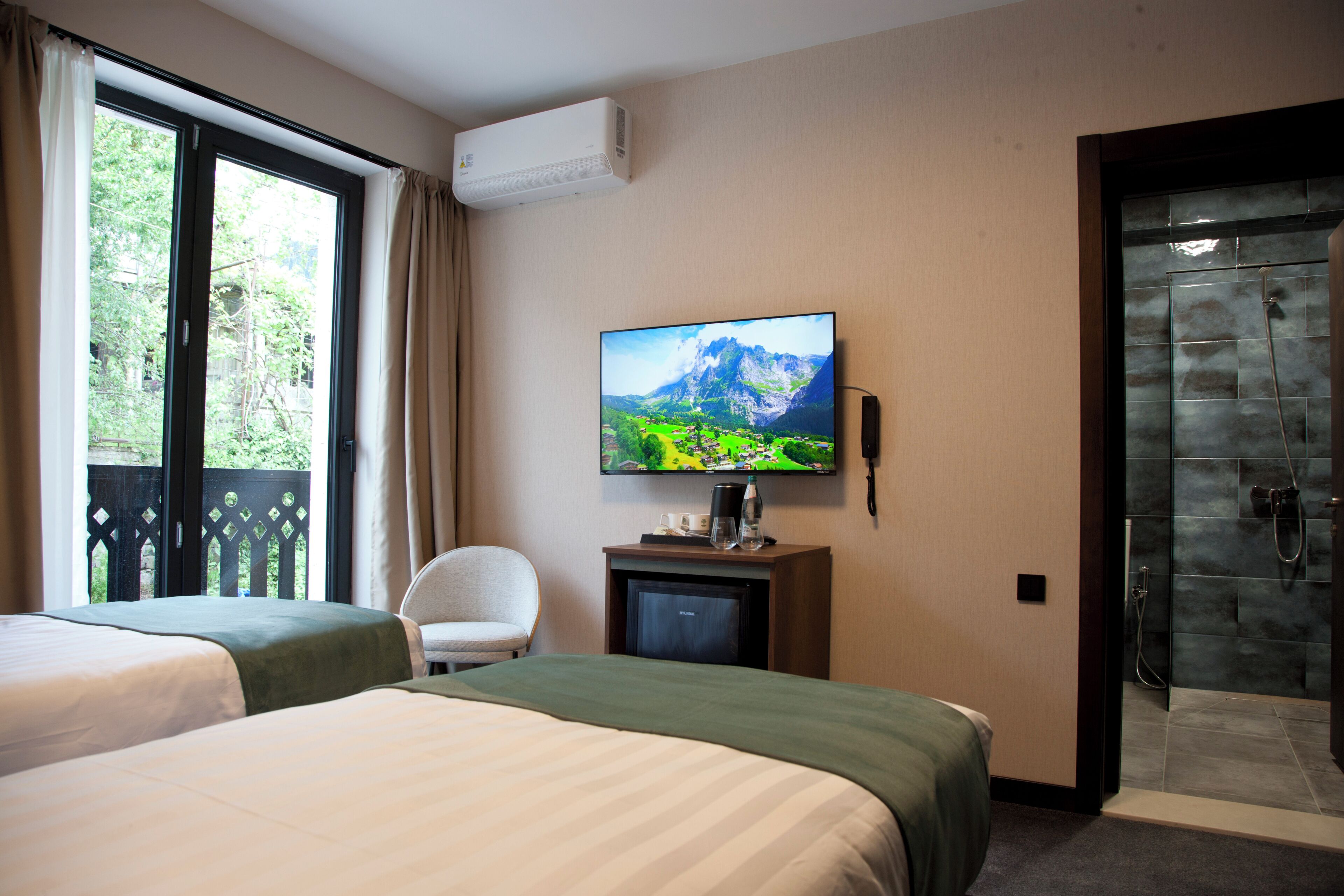A hotel room with two beds, a TV, a desk with a coffee maker, a chair, and a shower area.